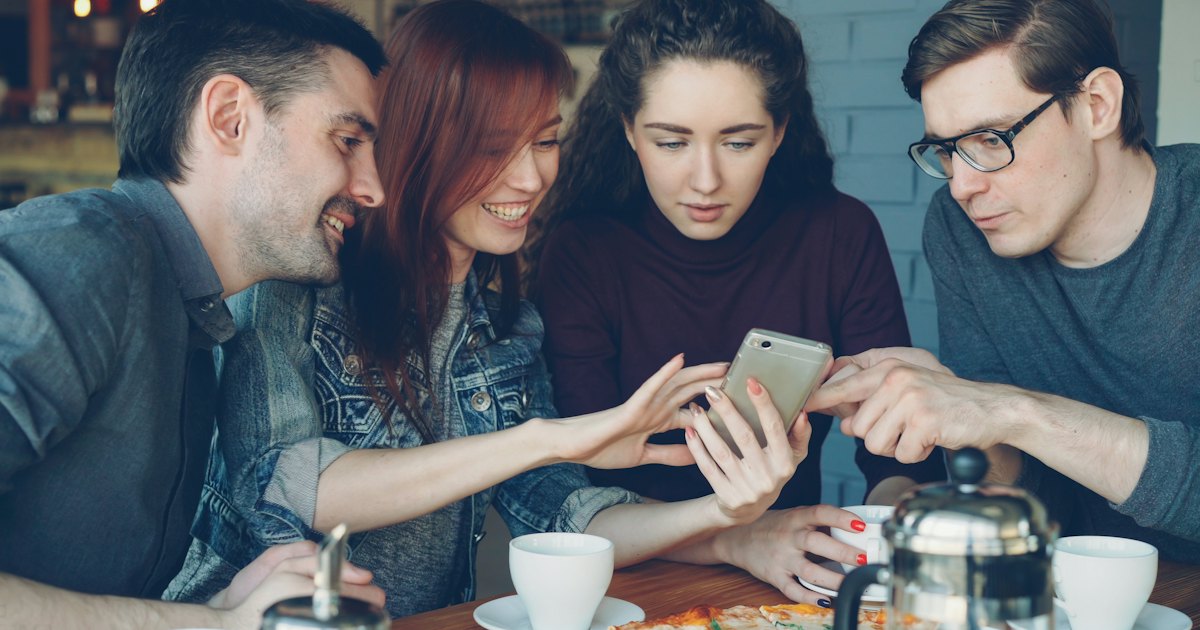 カフェのテーブルで友人たちが一台のスマートフォンを一緒に見ている様子